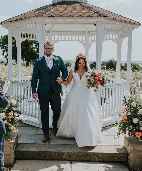 Bride in white dress and pink flower crown with groom at outdoor wedding at St Tewdrics House