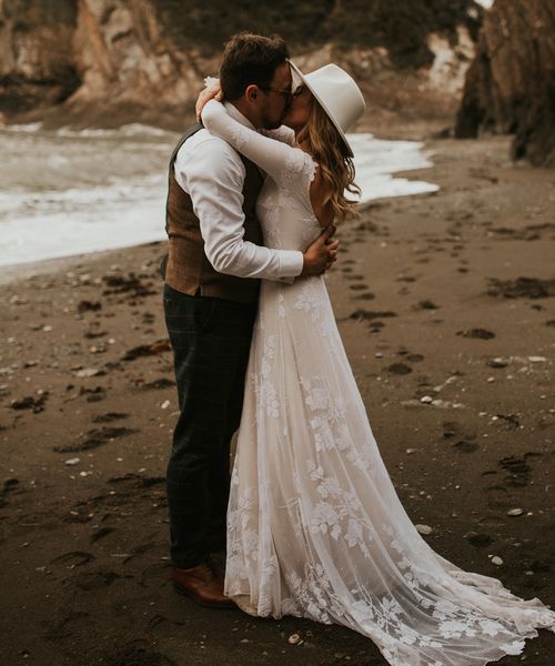 Seaside elopement with bride in a long sleeve lace wedding dress and fedora hat 