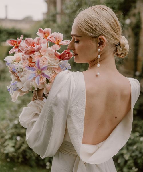 bride-in-open-back-wedding-dress-smelling-pink-wedding-bouquet-with-pearl-earrings