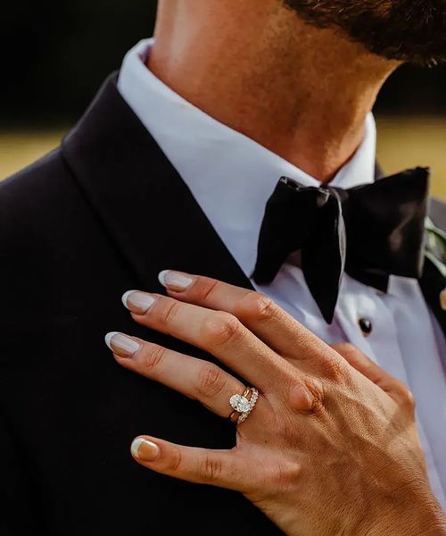 bride's hand on groom's chest with oval solitaire diamond engagement ring and chunky diamond wedding ring