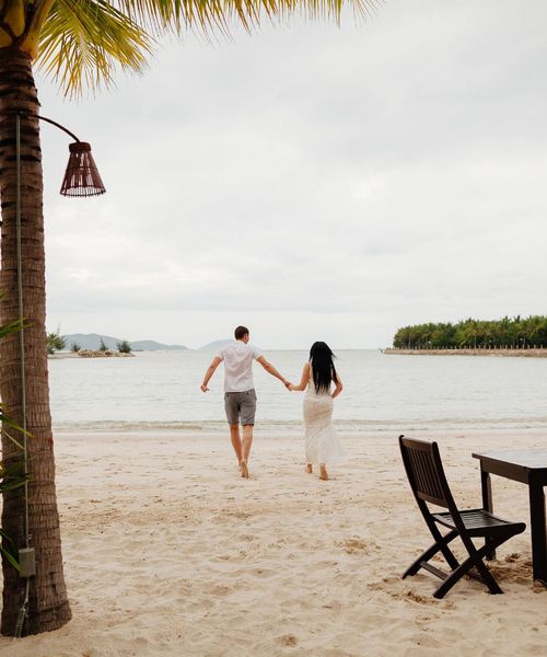 couple joyfully running along the beach towards the sea, celebrating their honeymoon