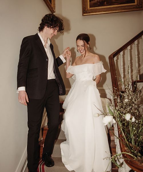 bride coming down the stairs with groom while wearing off-shoulder maxi wedding dress