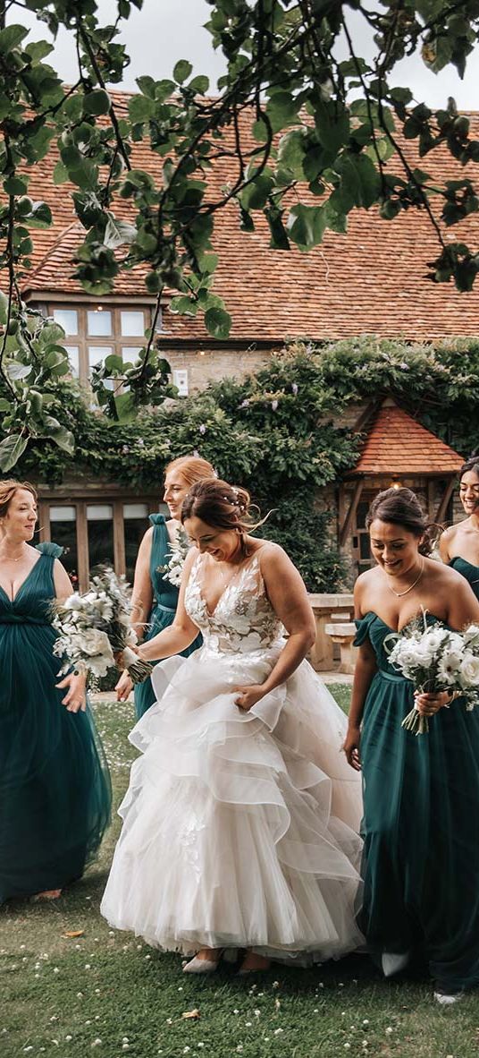 Bride in layered wedding dress walks with bridesmaids in green bridesmaid dresses