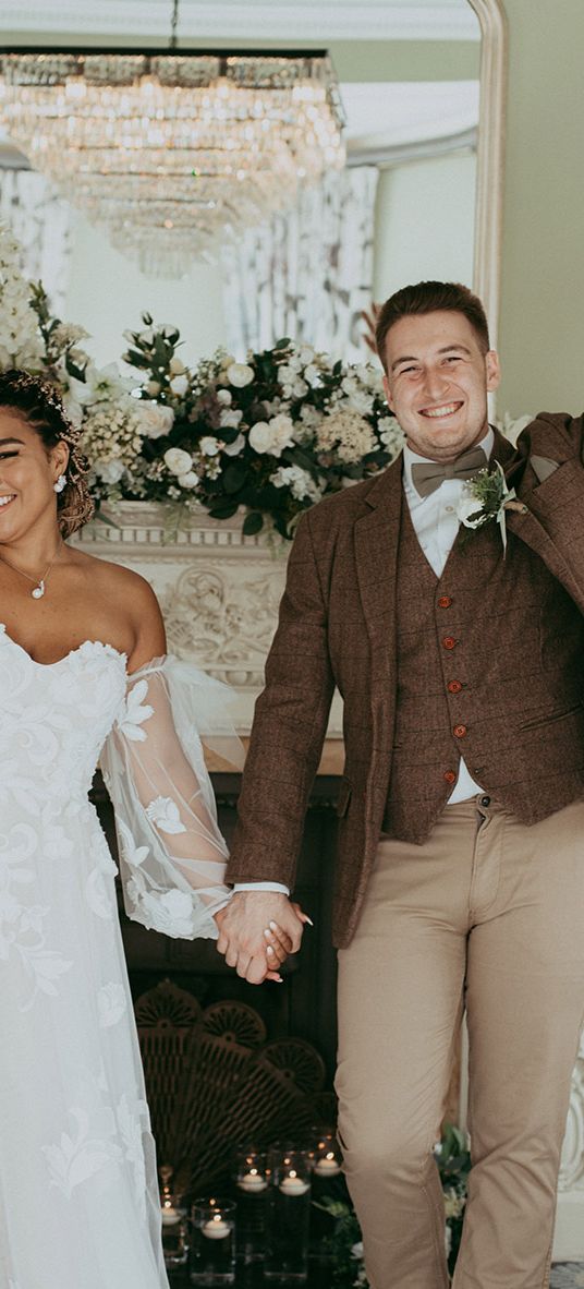 Bride in a floral wedding dress and the groom in a checkered suit in front of faux wedding flower decorations.