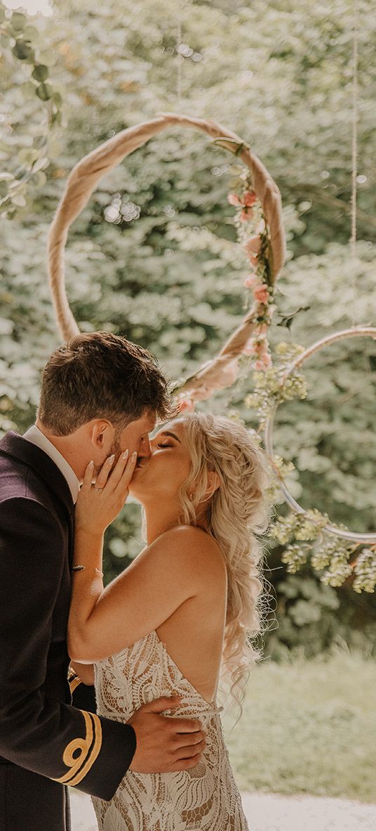 Hula hoop decor for the altar with the bride in a boho lace wedding dress kissing the groom in military uniform. 