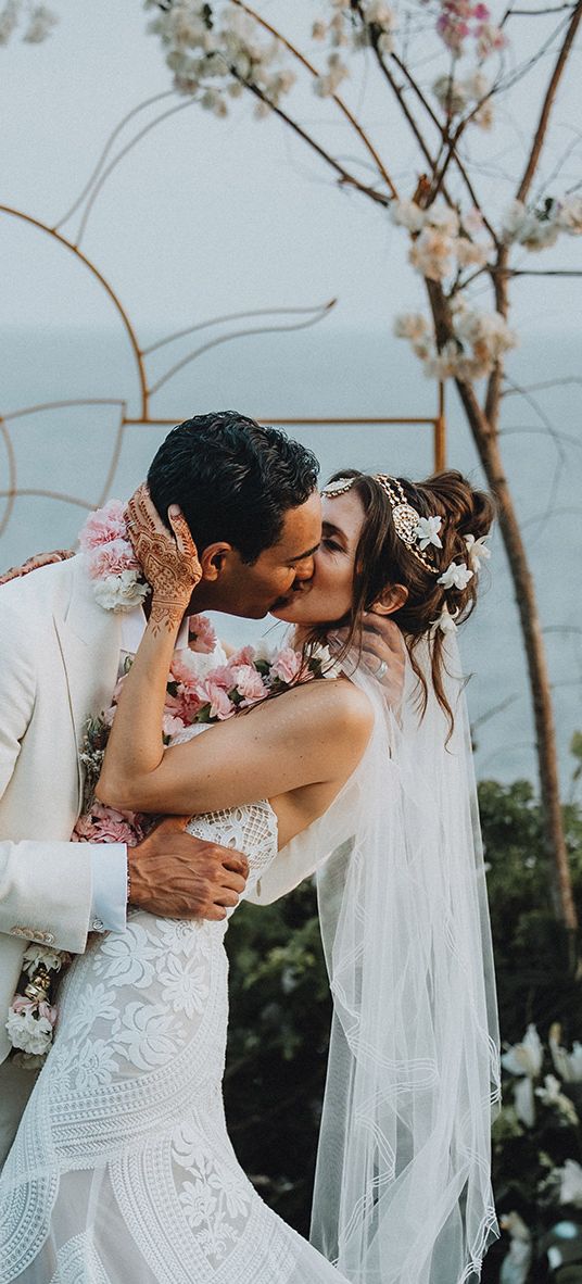 Groom in cream suit kisses bride in boho lace wedding dress and flower hair accessories at Tigre Del Mar wedding in Mexico