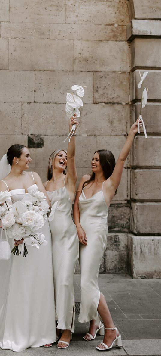 Bride holding white wedding bouquet with bridesmaids in white dresses.