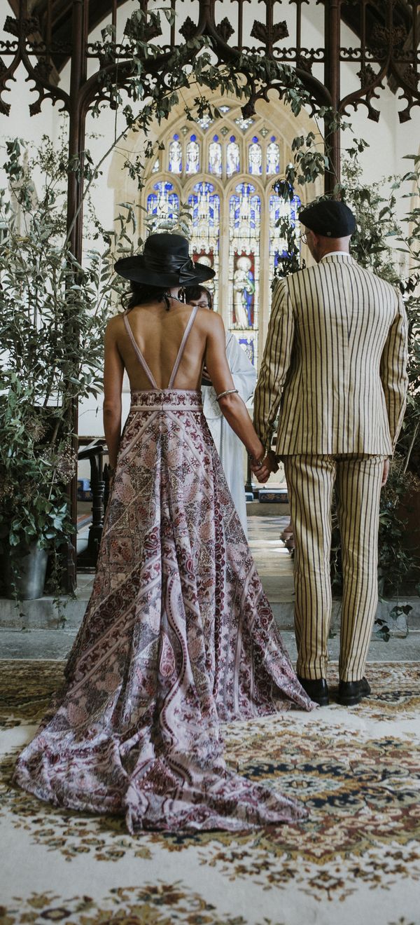 bride and groom wearing pink boho wedding dress and pinstripe groom suit stand at the altar facing away from guests