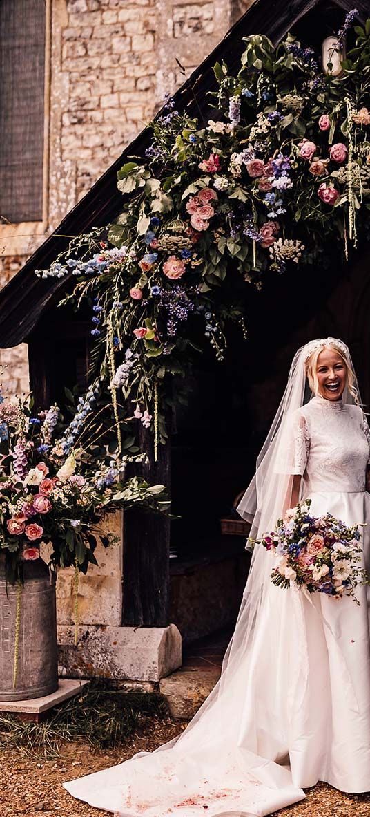 Bride in Jesus Peiro wedding dress and groom in suit stand in front of pink and blue wedding flowers display.