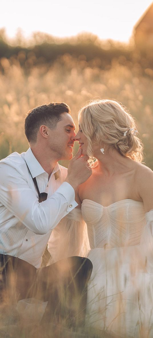 Bride and groom sitting in grass during golden hour at barn wedding