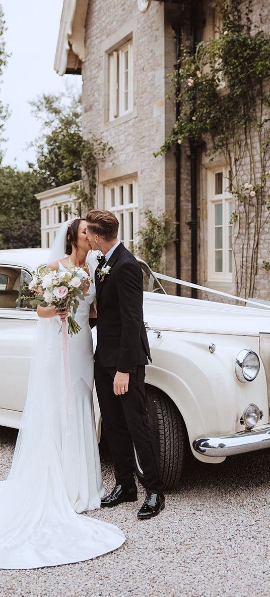 Bride and groom kissing in front of white wedding car at the Casterton Grange Estate venue.