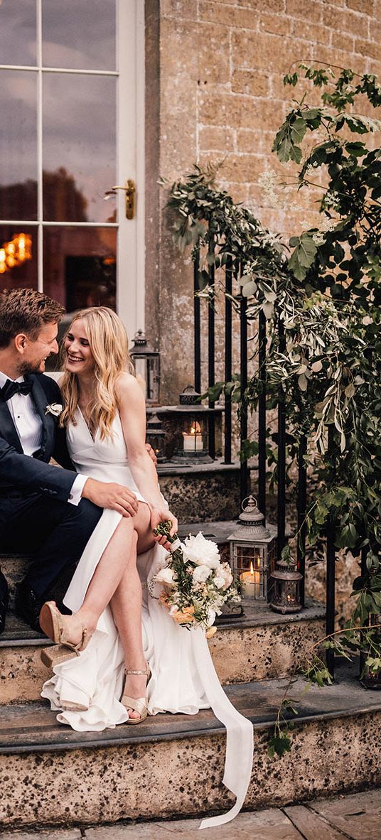 Bride and groom sit smiling on the stairs for their Babington House wedding.