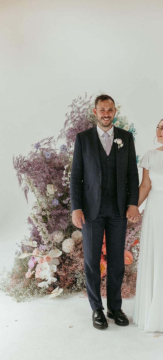 Bride and groom stand holding hands in front of pastel coloured wedding flower columns.