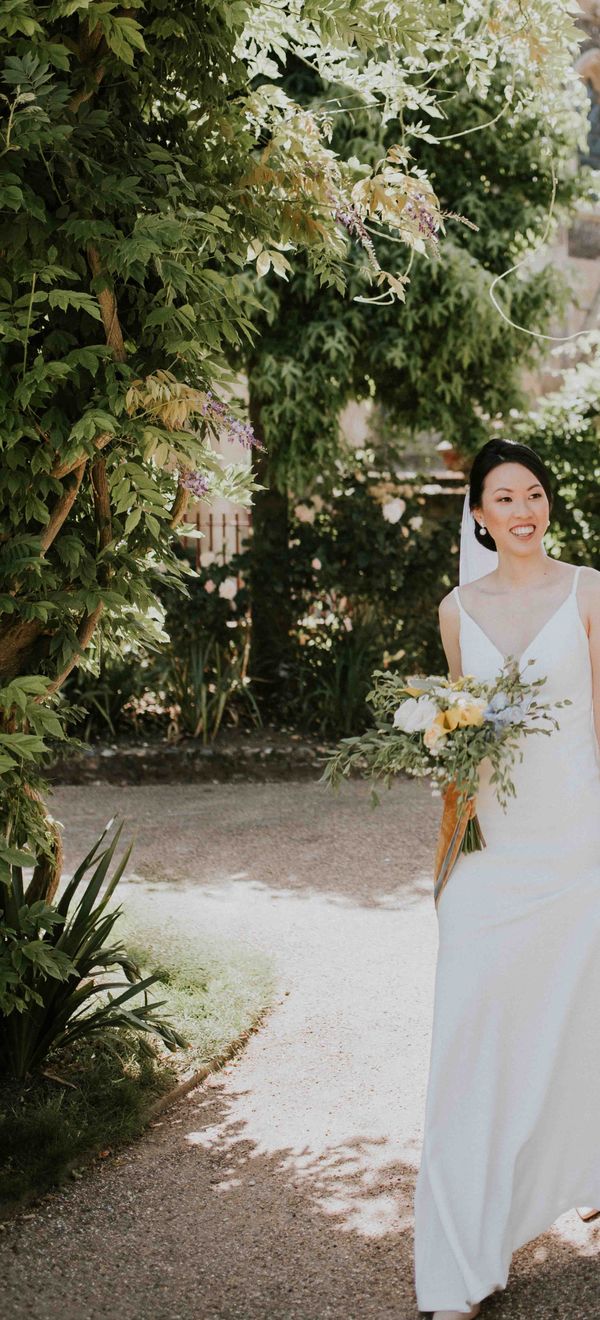 Bride and groom pose together outside their church wedding venue with blue and yellow colour palette as bride wears pearl hair pins and accessories