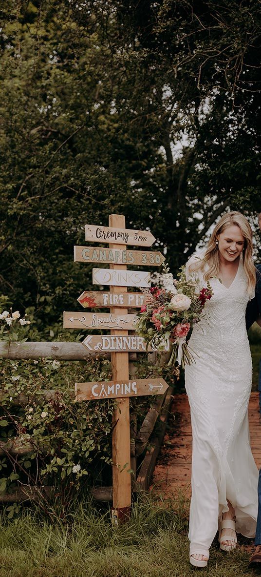 Bride and groom in front of their DIY wedding sign for rustic wedding at barn venue.