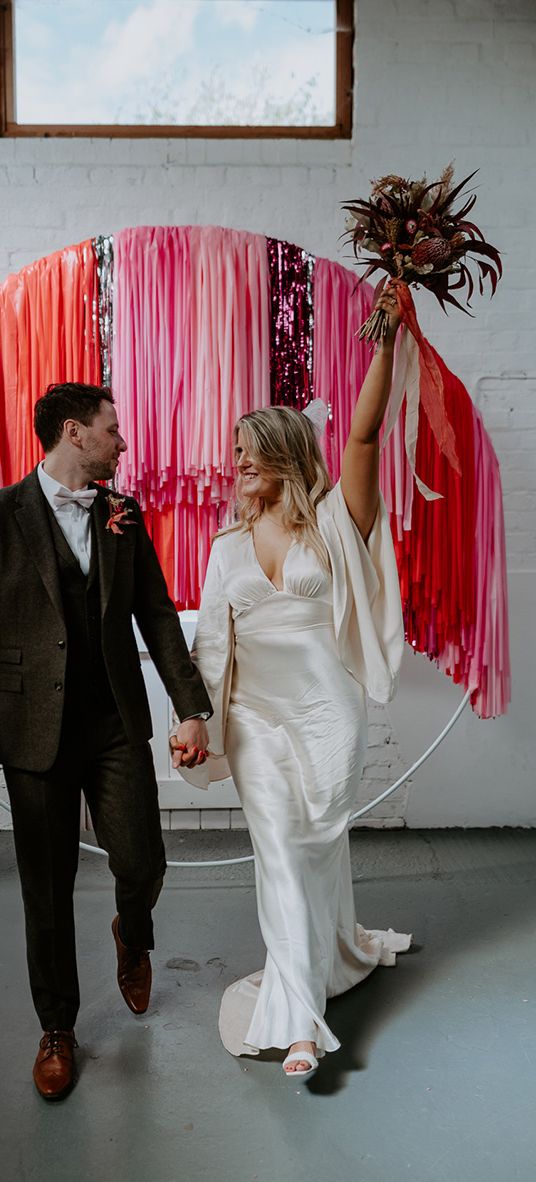 The bride and groom stand in front of pink, red and silver streamer decorations at the altar.