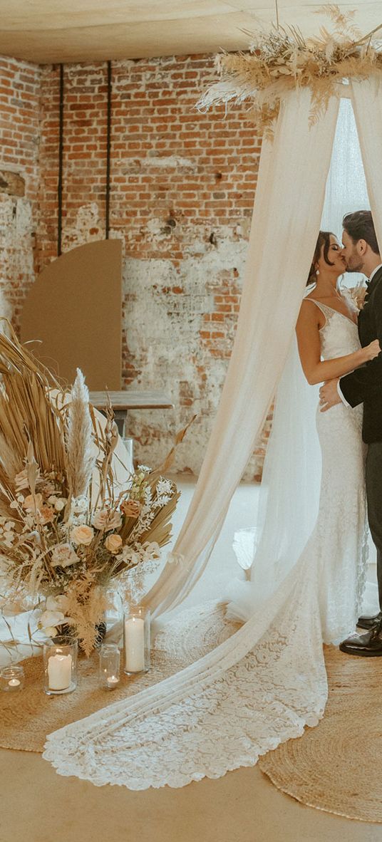 Bride and groom share a kiss under their wedding drapes at the altar decorated with candles at Godwick Barn. 