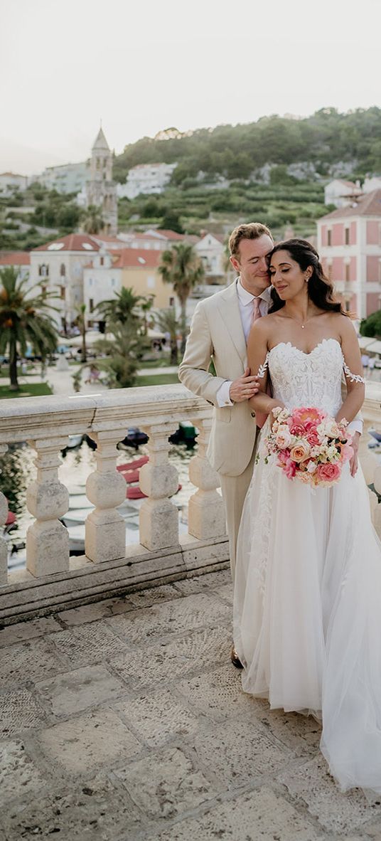 bride and groom stand on a balcony with Old Town Hvar in the background at destination wedding in Croatia 