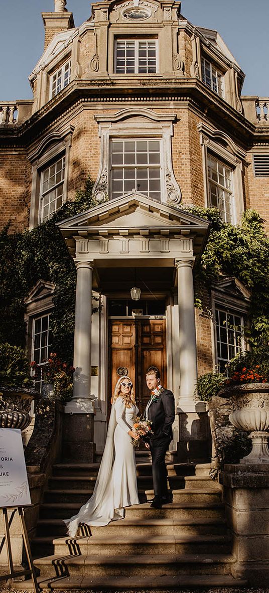 The bride and groom walk up the stairs at their wedding venue, Hampton Court House