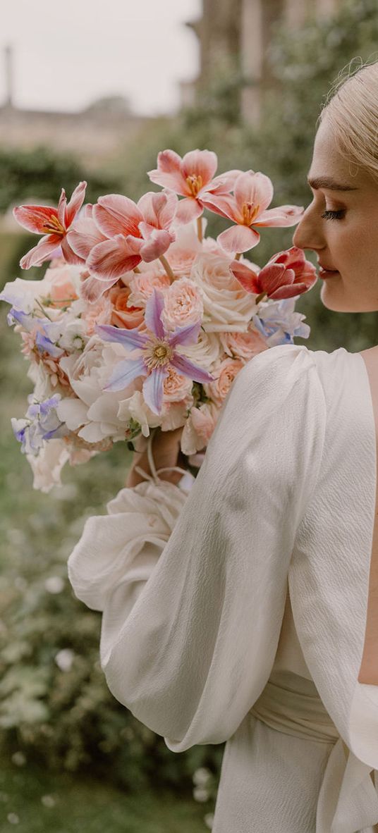 bride-in-open-back-wedding-dress-smelling-pink-wedding-bouquet-with-pearl-earrings