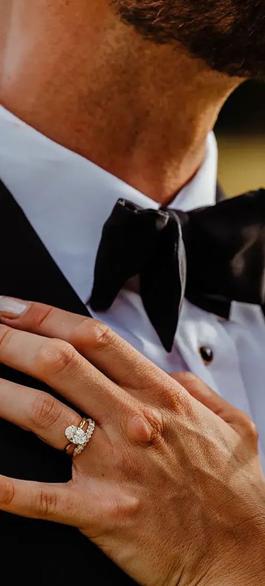 bride's hand on groom's chest with oval solitaire diamond engagement ring and chunky diamond wedding ring