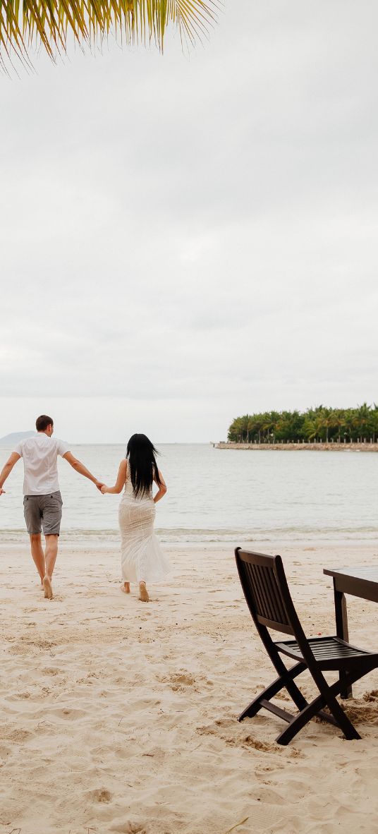 couple joyfully running along the beach towards the sea, celebrating their honeymoon