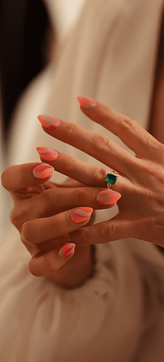 Bride wears almond shaped wedding nails with pink abstract wavy lines nail art with emerald engagement ring