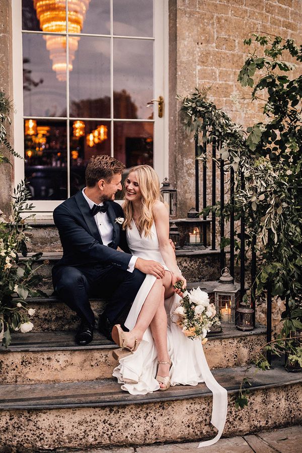 Bride and groom sit smiling on the stairs for their Babington House wedding.