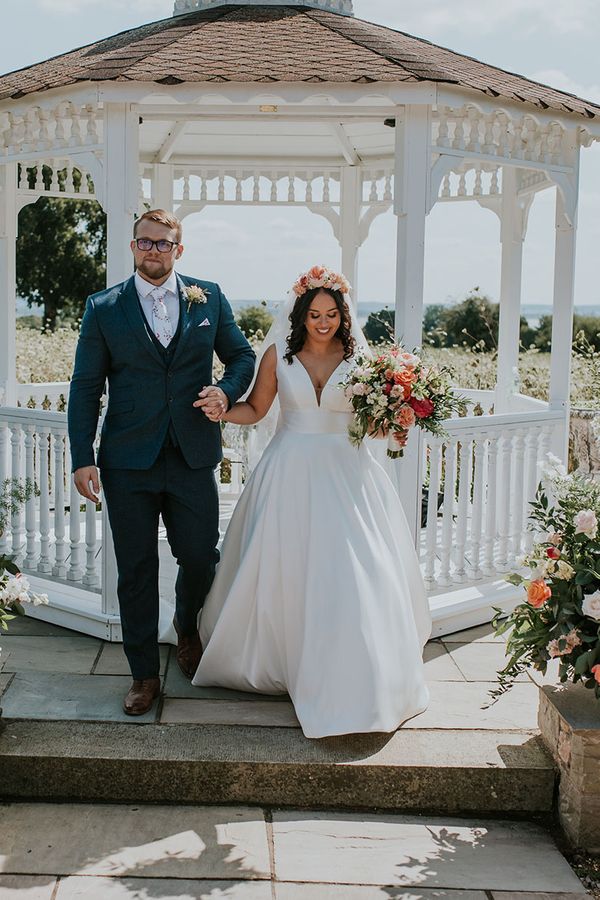 Bride in white dress and pink flower crown with groom at outdoor wedding at St Tewdrics House
