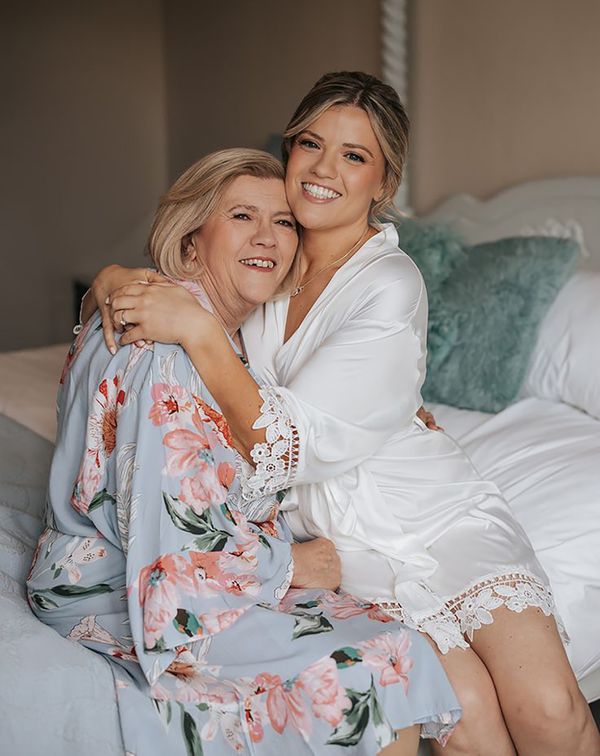 Bride and mother of the bride on wedding morning embracing in robes