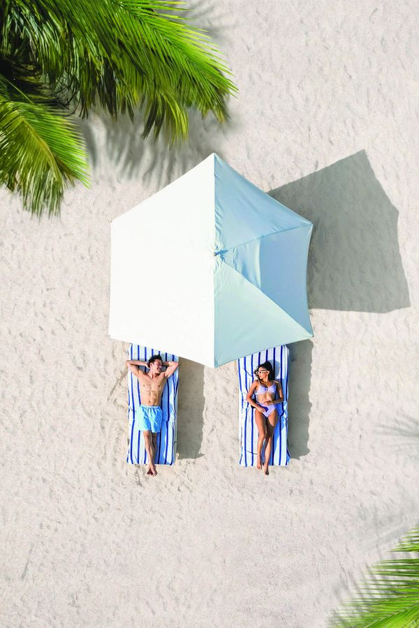 Couple relaxing on a white-sand beach under a parasol at a Sandals Resorts adults-only all-inclusive Caribbean honeymoon destination