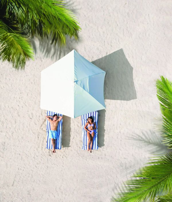 Couple relaxing on a white-sand beach under a parasol at a Sandals Resorts adults-only all-inclusive Caribbean honeymoon destination