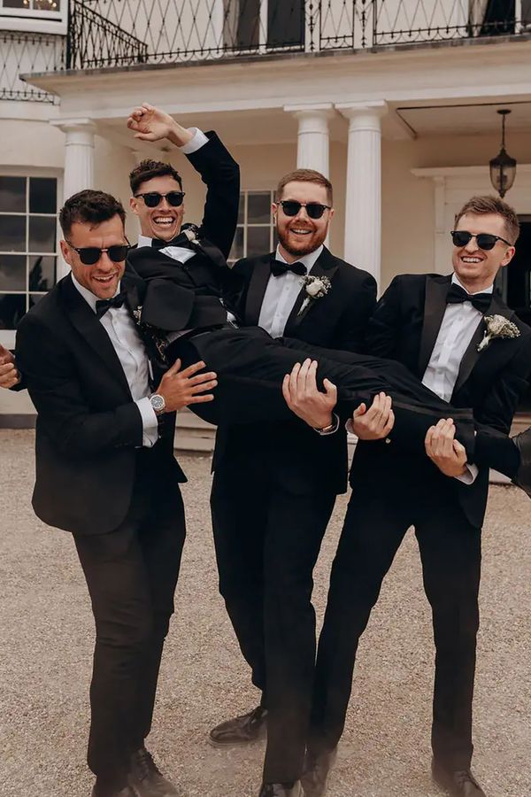 Groomsmen lifting groom in black tie tuxedos