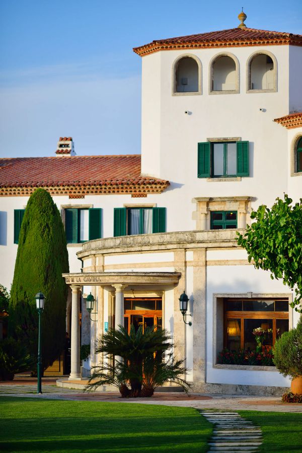 White Mediterranean-style exterior of Hostal de La Gavina in Costa Brava, Spain, featuring green shutters, gardens and elegant architecture at sunset for the perfect honeymoon hotel in Spain 