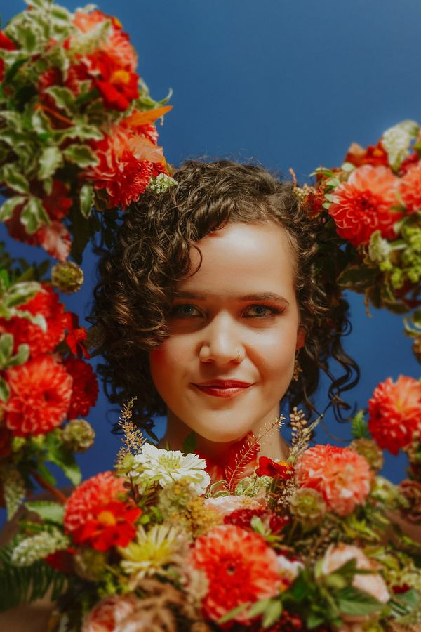 Bride with glowing skin and bridesmaids holding coral dahlia wedding bouquets around her face