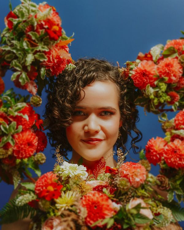 Bride with glowing skin and bridesmaids holding coral dahlia wedding bouquets around her face