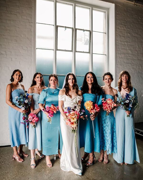 Bridal party wearing mismatched blue bridesmaid dresses with colourful bouquets