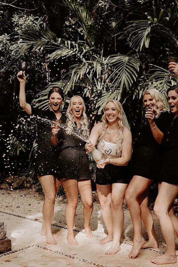Bridal party wearing matching black pjs spraying champagne for hen do