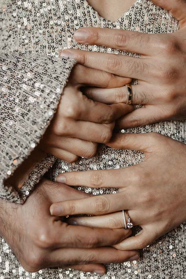 Couple holding hands across silver sparkly wedding dress with engagement rings