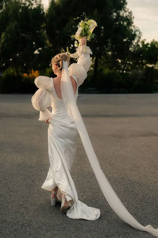 Bride wearing vintage style puff sleeve wedding dress holding bouquet in the air