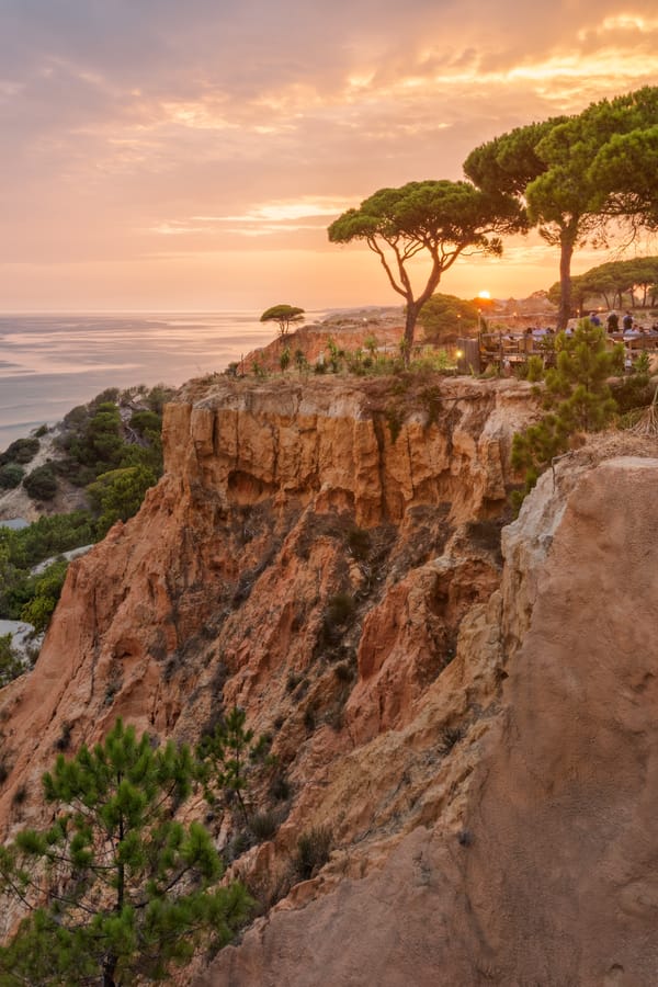 Sunset over the Atlantic Ocean at Pine Cliffs Resort in the Algarve, Portugal, featuring dramatic golden cliffs, pine trees and a scenic clifftop terrace overlooking the coastline.