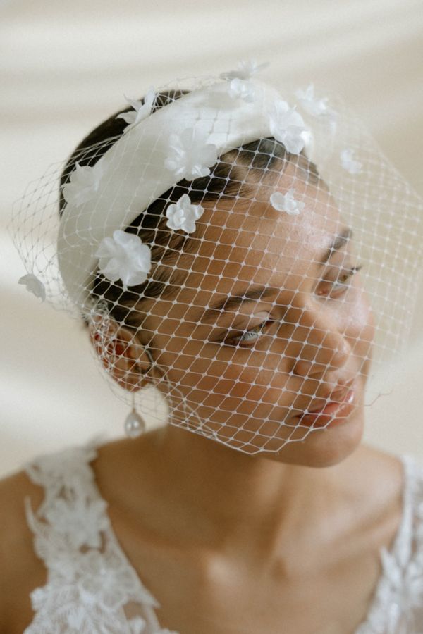 Bride wears an ivory birdcage wedding veil with 3d flowers and an ivory padded headband
