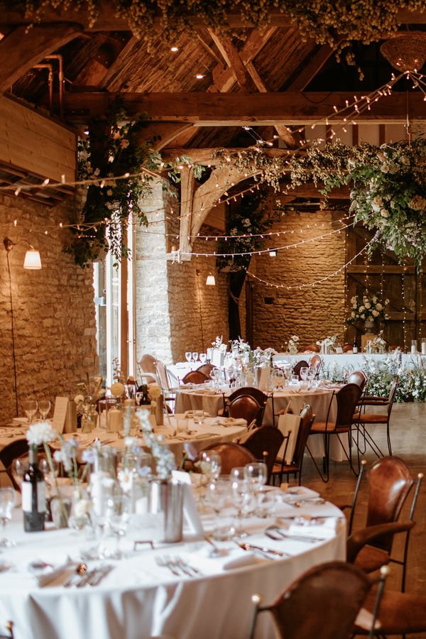 A summer barn wedding breakfast with round tables, white tablecloths and beautiful muted florals. By Kayley Bull Photography.