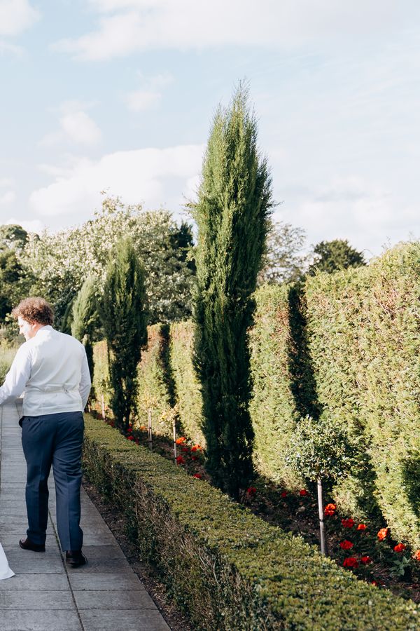 Modern romance meets classic English charm, the couple wander through a serene garden aisle moments after saying “I do”. Photography by Kseniia Photo.