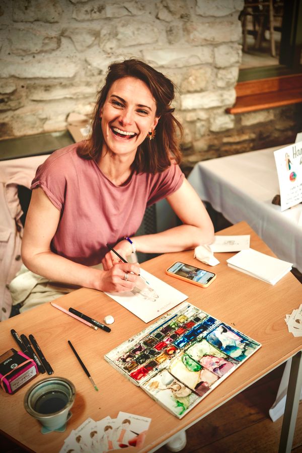 Jo smiling happily whilst painting portraits with watercolours. Photo by Adam Jervis Photography 