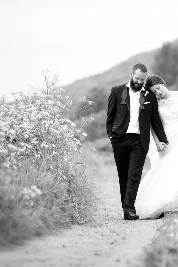 Bride in white dress walks hand in hand with groom in relaxed black tie along a country lane photographed by Russell Lewis Photography