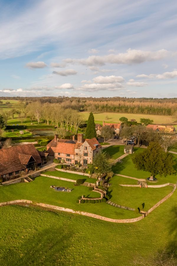 A stunning aerial view of Burrow Farm Estate, showcasing the beautifully restored main house and barn nestled within rolling countryside, surrounded by manicured gardens, woodland and expansive open fields in the heart of the Chiltern Hills. Image credit: Burrow Farm Estate