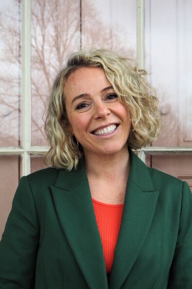 A headshot of a smiling blonde woman wearing an orange top and a green jacket taken at Clissold House in East London by Hannah Eachus 