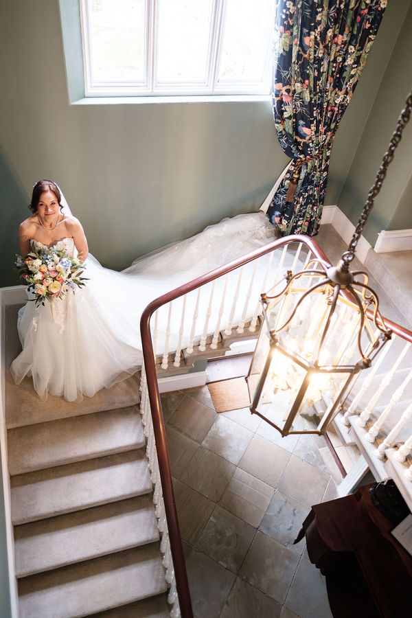 A bride in a flowing white dress descending the stairs of Dunston Hall taken by 21 Photography
