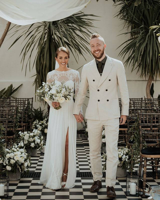 bride in lace Catherine Dean wedding dress with white wedding bouquet stands with husband in beige suit at Gunnesbury Park Orangery wedding altar